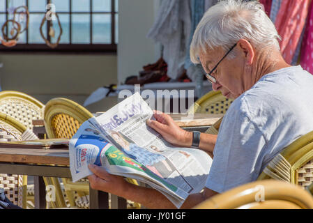 Matura, maschio caucasico leggendo un giornale sul lungomare, Herne Bay, Kent. Foto Stock