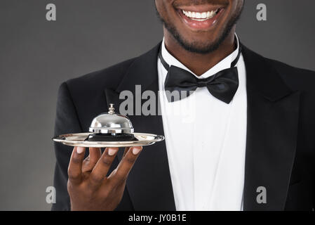 Ritratto di Felice cameriere africano Holding campana di servizio Foto Stock