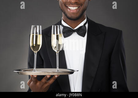 African cameriere azienda bere champagne su sfondo nero Foto Stock