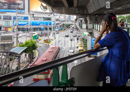 Giovane donna sul telefono cellulare stavano in piedi su un ponte pedonale che si affaccia su Sukhumvit Road, Bangkok, Thailandia Foto Stock