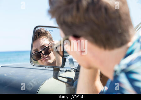 La riflessione di uomo caucasico in vista laterale specchio di auto sulla spiaggia Foto Stock