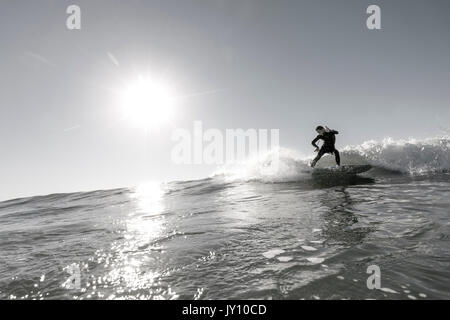 Distante uomo caucasico surf nella soleggiata ocean Foto Stock