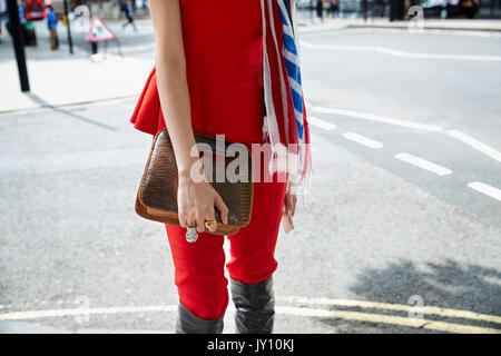 La donna nella parte superiore rossa e pantaloni con un coccodrillo marrone borsa in pelle Foto Stock