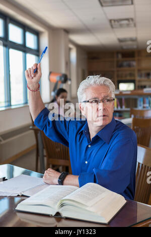 Uomo più anziano nella libreria alzando la mano e domande Foto Stock