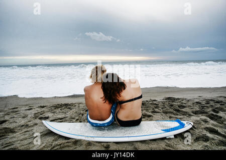 Caucasian giovane seduto sulla tavola da surf in spiaggia Foto Stock