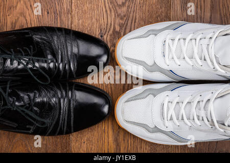 Angolo di Alta Vista della coppia di bianco e nero scarpe disposti sul pavimento in legno Foto Stock