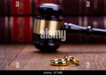 Close-up di anelli di nozze con il martello sulla scrivania di legno nelle aule di tribunale Foto Stock