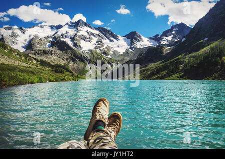 Traveler in appoggio su di un altopiano di montagna. POV view, gambe close up sullo sfondo del paesaggio di montagna con un bellissimo lago turchese Foto Stock