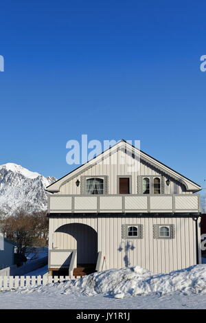 White cottage di legno con corridoio e terrazzo e circondato da recinzione bianco-snowy Reine villaggio in inverno. Festhaeltinden mountain in background. Foto Stock