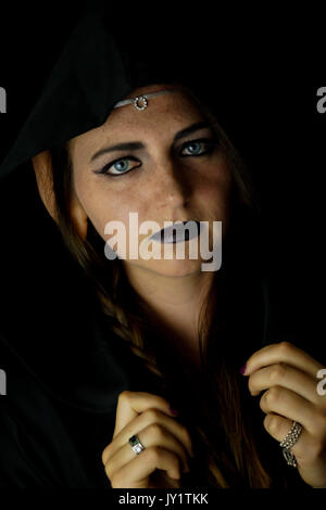 Una giovane donna vestita come un elfo nero con un accappatoio con cappuccio e capelli lunghi con sottolineato elf orecchie Foto Stock