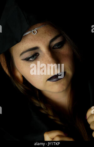 Una giovane donna vestita come un elfo nero con un accappatoio con cappuccio e capelli lunghi con sottolineato elf orecchie Foto Stock