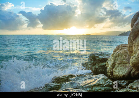 Splash le onde battono le rocce con il bellissimo tramonto e il cielo . Foto Stock
