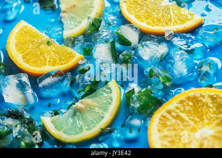 Close-up di fettine di arance e di limoni su uno sfondo blu con cubetti di ghiaccio Foto Stock