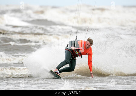 Southport, Merseyside, 19 agosto 2017. Regno Unito Meteo. Davvero un ventoso e molto più freddo giorno con alcuni pesanti Scattered Showers non scoraggiare questo kite boarder da equitazione il surf sulla marea a Southport nel Merseyside. Credito: Cernan Elias/Alamy Live News Foto Stock