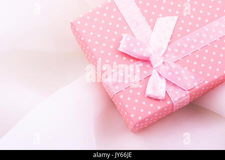 Rosa confezione regalo legato con nastro di raso con fiocco sul delicato tessuto bianco sullo sfondo, romantico, San Valentino, Festa della mamma, natale, presente, modello CO Foto Stock