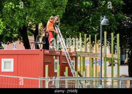 Kristiansand, Norvegia - 1 Agosto 2017: documentario della vita quotidiana nella città. Operaio edile sul tetto toolshed avvolgimento di un cavo elettrico. Ladde Foto Stock