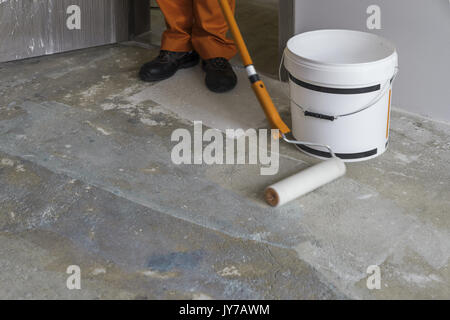 Appartamento in costruzione. Lavoratore mette il primer con il rullo del pavimento in calcestruzzo Foto Stock