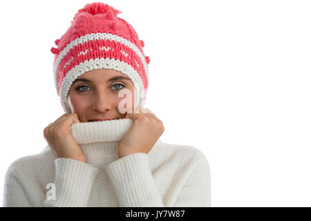 Ritratto di donna che indossa knit hat mentre ricopre la faccia con turtleneck maglione contro uno sfondo bianco Foto Stock