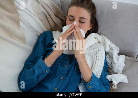 Elevato angolo di visione della donna strofinando il naso mentre sdraiato sul divano di casa Foto Stock