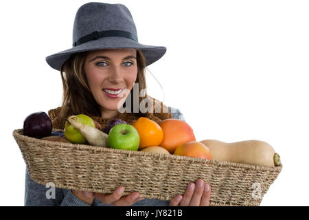 Ritratto di giovane donna tenendo le verdure in cesto in vimini mentre in piedi contro uno sfondo bianco Foto Stock