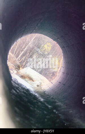 Canale sotterraneo - scarico sotto la strada per il piccolo fiume. Grosso tubo sotto l'AUTOSTRADA, AUTOSTRADA ingegneria; roadmaking. In corrispondenza dell'altra estremità del tubo di legno visibile Foto Stock