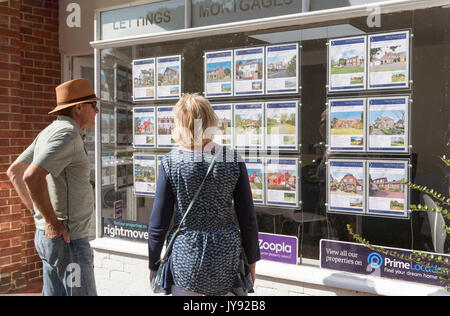 Coppia in cerca di un agente immobiliare la finestra alla proprietà in vendita. Inghilterra, Regno Unito Foto Stock