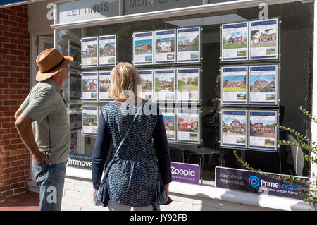 Coppia in cerca di un agente immobiliare la finestra alla proprietà in vendita. Inghilterra, Regno Unito Foto Stock