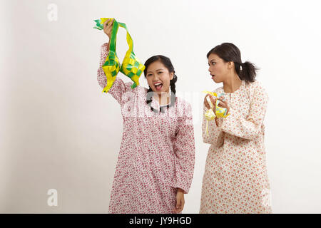 Due donna malay indossando baju kedah holding ketupat sullo sfondo bianco Foto Stock