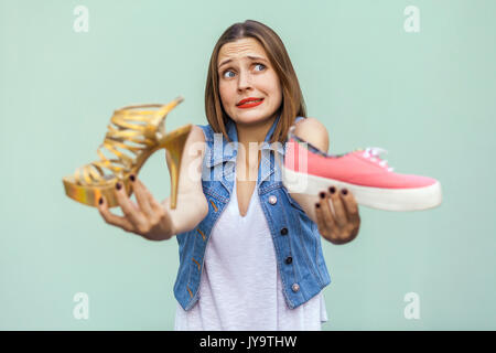 La bellissima ragazza con le lentiggini in mall ha ottenuto la scelta di sneakers o scarpe di bello, di pensare e di guardare in su. Isolato studio shot sul verde chiaro backgro Foto Stock