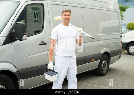 Felice pittore matura in piedi nella parte anteriore del furgone Foto Stock