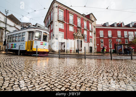 Il giallo il tram numero 28 passa nel quartiere di Alfama caratterizzato da una tipica architettura in un giorno di pioggia Lisbona Portogallo Europa Foto Stock