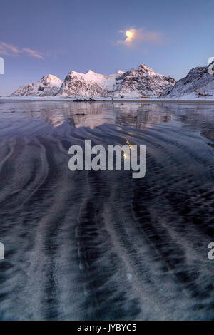 Le onde e il ghiaccio nel surreale Skagsanden spiaggia circondata da vette innevate Flakstad Nordland county Isole Lofoten in Norvegia Europa Foto Stock