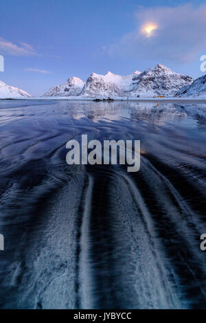 Le onde e il ghiaccio nel surreale Skagsanden spiaggia circondata da vette innevate Flakstad Nordland county Isole Lofoten in Norvegia Europa Foto Stock