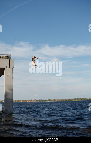 Un uomo è il salto in mare da un molo di alta. Adrenalina e extreme. Back flip salto. Foto Stock