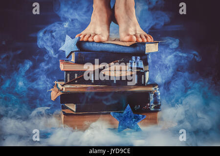 Bambino in piedi su una pila di libri nel mezzo di una nuvola di fumo. dark ancora la vita in sfumature di blu. istruzione metafora. Foto Stock