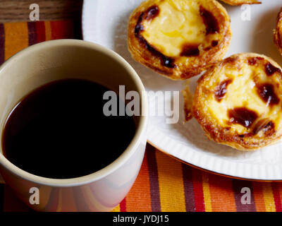 Crema pasticcera crostate in una piastra e un nero tazza da caffè Foto Stock
