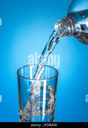 Una bottiglia versando acqua in un bicchiere con il blu Foto Stock