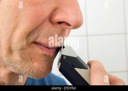 Close-up di un uomo di rifinitura di baffi con trimmer Foto Stock