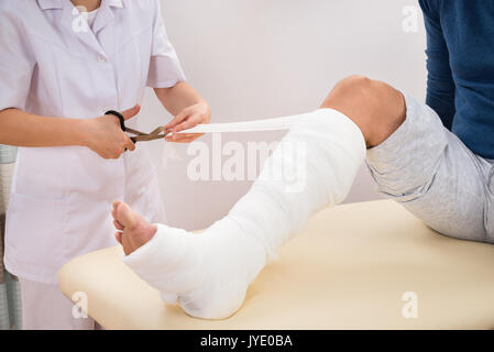 Ritratto di donna medico del bendaggio gamba del paziente in Clinica Foto Stock