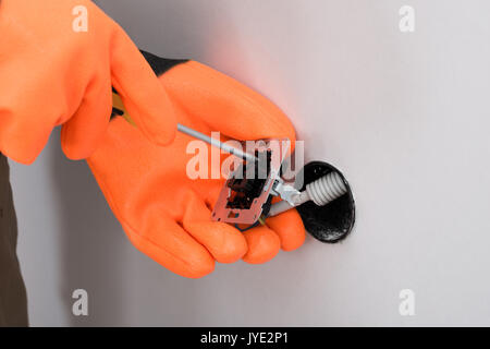 Close-up di un elettricista che indossa guanti presa di fissaggio con un cacciavite sulla parete Foto Stock