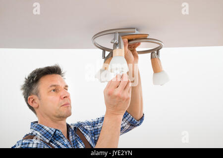 Ritratto di un elettricista maschio che fissa la luce sul soffitto Foto Stock