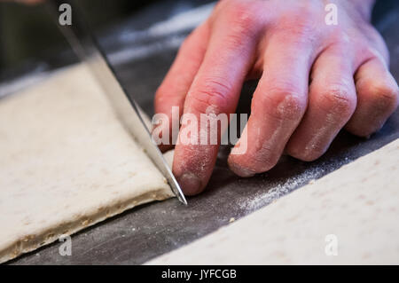 Uno chef che taglia la pasta per la produzione di grissini italiano Foto Stock