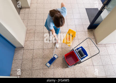 Femmina con straccio bidello di piano con attrezzature di pulizia e pavimento bagnato segno sul pavimento Foto Stock