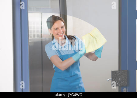 Giovani felici bidello femmina pulire il vetro con un panno Foto Stock