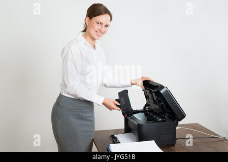 Giovane imprenditrice felice tenendo la cartuccia laser con stampante a scrivania Foto Stock