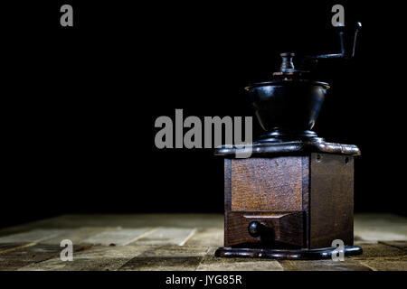 Vecchio macinino elegante per la macinazione di gustosi caffè su un vecchio tavolo di legno, sfondo nero Foto Stock