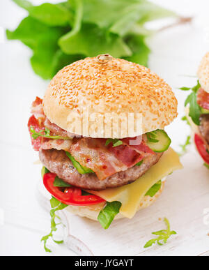 Grande panino - hamburger burger con carne, formaggio, pomodori, cetrioli e pancetta fritta. Foto Stock