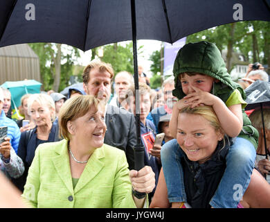 Ahrenshoop, Germania. 19 Ago, 2017. Il cancelliere tedesco Angela Merkel (CDU) mantiene il suo ombrello al di sopra di una donna e suo figlio di fronte al museo di arti in Ahrenshoop, Germania, 19 agosto 2017. Merkel ha aperto il XVIII Lunga Notte Delle Arti in Ahrenshoop. Il cancelliere è sponsor nel '125 anno giubilare della Ahrenshoop colonia di artisti". Foto: Axel Heimken/dpa/Alamy Live News Foto Stock