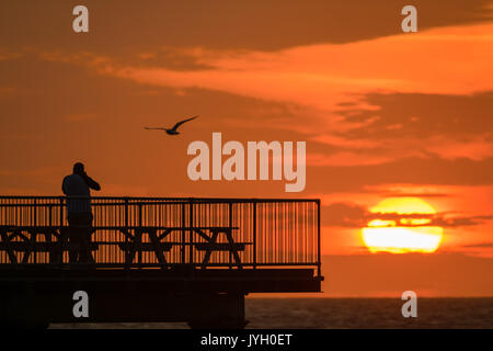 Aberystwyth Wales UK, sabato 19 agosto 2017 UK Meteo: alla fine di una giornata di vento blustery e docce di pioggia, un uomo in piedi alla fine della città il Royal Pier ottiene la possibilità di fotografare il tramonto dorato in Aberystwyth Wales. Photo credit: Keith Morris/Alamy Live News Foto Stock