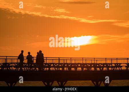 Aberystwyth Wales UK, sabato 19 agosto 2017 UK Meteo: alla fine di una giornata di vento blustery e docce di pioggia, le persone in piedi alla fine della città il Royal Pier di avere la possibilità di godere di un tramonto dorato in Aberystwyth Wales. Photo credit: Keith Morris/Alamy Live News Foto Stock